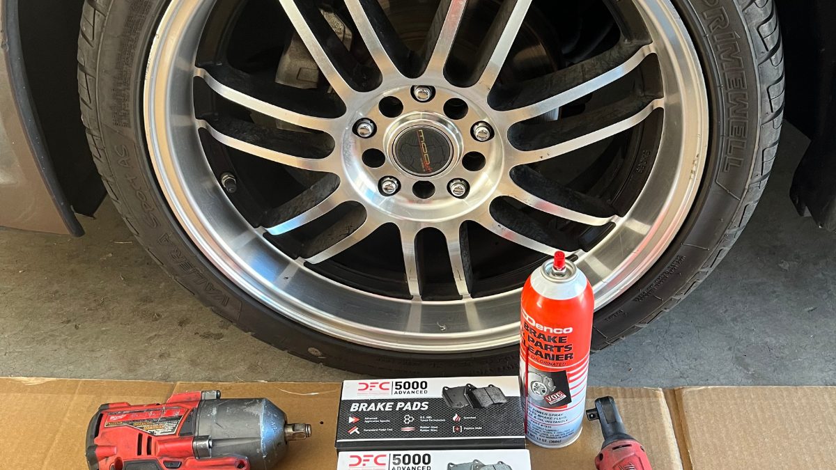 New brake pads, brake cleaner and an impact wrench next to a wheel